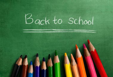 Yeşil zemin üzerinde okula dönüş metni olan renkli kalemler