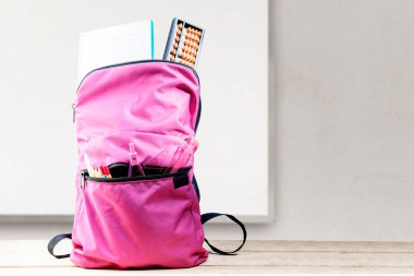 Sırt çantasında kitap ve tahta bir masa ve beyaz tahta bir arka plan var. Okul konseptine dönüş