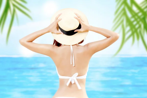 Rear view of Asian woman with bikini and hat relaxing on the beach