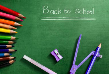 Yeşil zemin üzerinde okula dönüş metni olan renkli kalemler ve kırtasiye malzemeleri