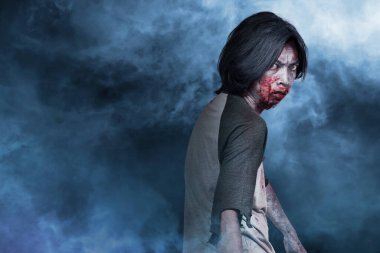 Vücudunda kan ve yara olan korkunç zombi dumanlı arka planda duruyor.