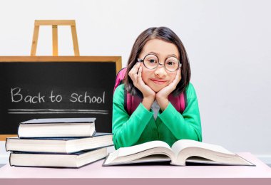 Gözlüklü Asyalı küçük kız sınıfta kitap okuyor. Okul konseptine dönüş