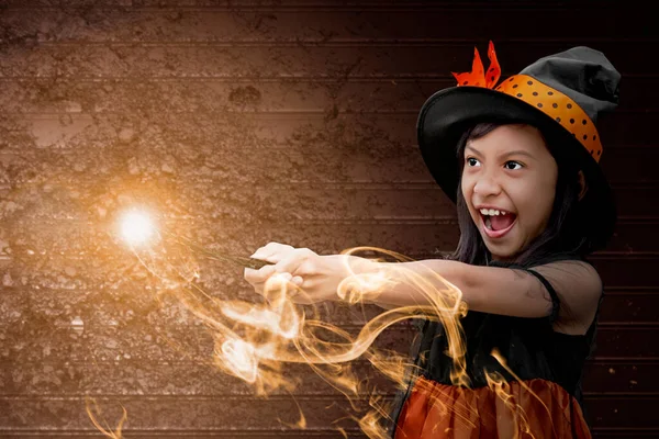 亚洲女巫小女孩用魔杖 用魔法般的光芒 用神秘的火把 并配上发牢骚的墙背景 — 图库照片