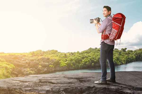 一个背着背包拿着相机的亚洲人 带着湖景和蓝天背景 世界旅游日 — 图库照片