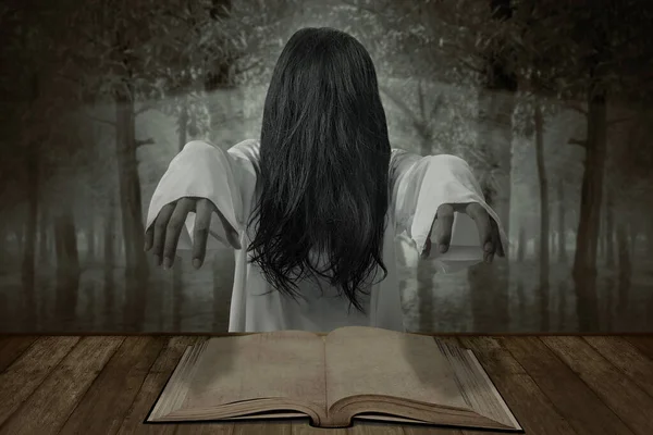 Scary ghost woman standing with a book on the table in the forest. Halloween concept