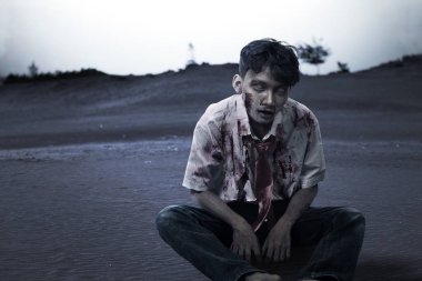 Sahada oturan, üzerinde kan ve yara olan korkunç zombi.