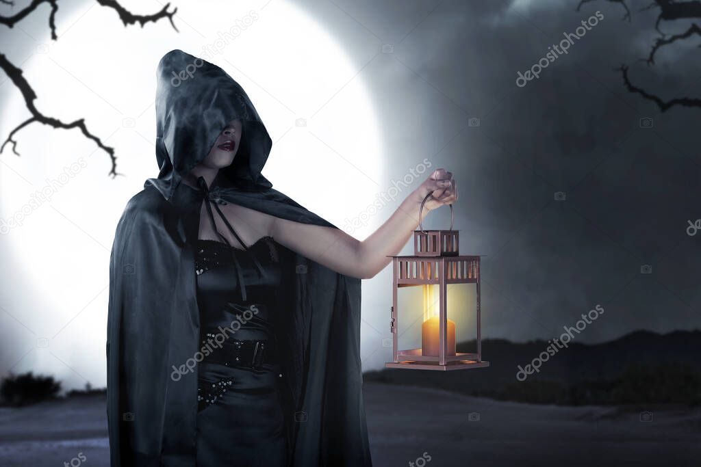 Asian witch woman with a black cloak holding a lantern standing with a night scene background