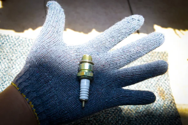 Hand with glove holding spark plug with blurred background