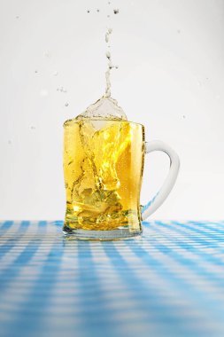 Mavi kareli masa örtüsü üzerine sıçramış bira bardağı ya da beyaz bir masanın üzerindeki peçete. Ekim Festivali kavramı. Bavyera Alman kültür festivali dekorasyon sembolü