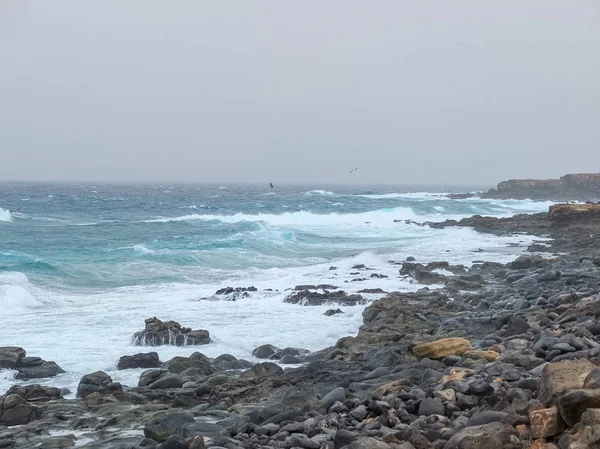 The black rocks and shoreline of Lanzarote in Spain during a wind storm that caused sea spray as the waves hit the shoreline.