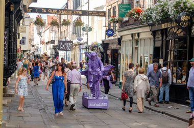 Stonegate, York, England, UK - August 05, 2011: The Stonegate in York City Centre packed with holiday makers and visitors looking in windows of shops and cafes. and in particular the 'Purple Man Statue' often seen arround the city centre in summer. clipart