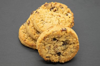 Meyveli ve yulaflı kurabiyeler siyah tahtada, fırından yeni çıkmış ve yemeye hazır. Öndeki kurabiyeye odaklan.