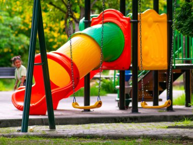 Boş çocuk parkı salıncağı yemyeşil ağaçlarla dolu. Nostaljik çocukluk anıları ve barışçıl açık hava eğlence ekipmanları..