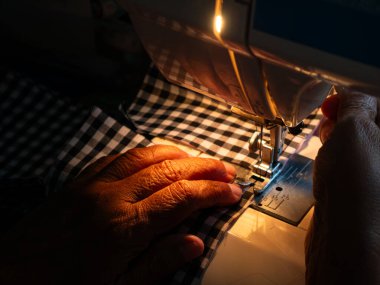 Yaşlı kadın elleri elektrikli dikiş makinesiyle kumaş dikiyor. Kıdemli İşçi ve El Sanatları.