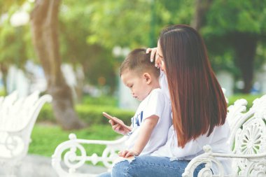 Küçük çocuk konsantre smartphone ile onun anne oturup birlikte parkta.