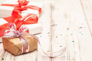 Arka plan metin için yer ile yönetim kurulu bir kahverengi hediye kutusu ve iki beyaz kağıt kutusu beyaz tahta üzerine kırmızı kurdele ile.