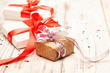 Arka plan metin için yer ile yönetim kurulu bir kahverengi hediye kutusu ve iki beyaz kağıt kutusu beyaz tahta üzerine kırmızı kurdele ile.