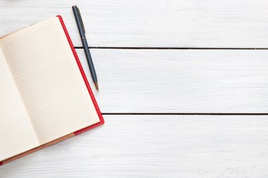 Beyaz ahşap masa üzerinde kırmızı açık not defteri ve kalem. Üstte görüntü.