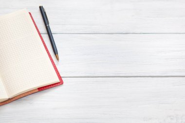 Beyaz ahşap masa üzerinde kırmızı açık not defteri ve kalem. Üstte görüntü.