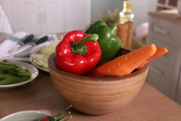 a red and a green bell pepper and peel carrot put in wooden bowl in the kitchen