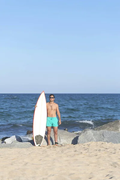 年轻有吸引力的冲浪手拿着他的冲浪板在海滩上穿着绿色泳装 — 图库照片
