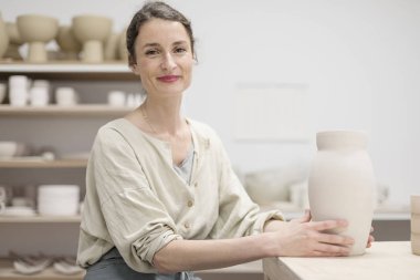 Genç kadın tablosu tarafından oturma ve çalışma stüdyosunda kil veya seramik kupa yapma