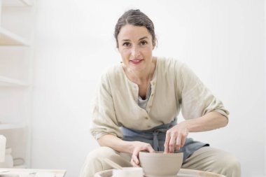 Genç kadın tablosu tarafından oturma ve çalışma stüdyosunda kil veya seramik kupa yapma