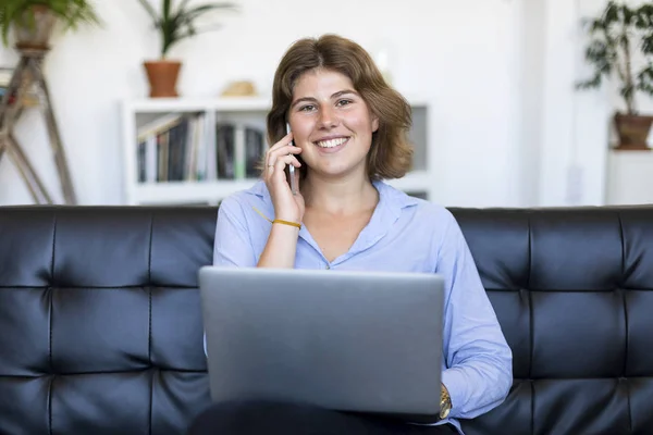 Entrepreneur woman wearing blue shirt working with a laptop sitting on a couch at home