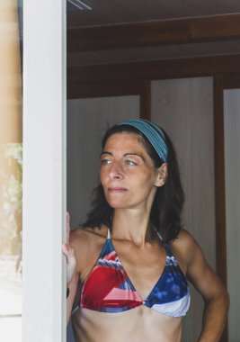 Genç kadın portre mayo ve taç giyen ve uzağa arıyorsunuz bir kapı tarafında yaslanmış