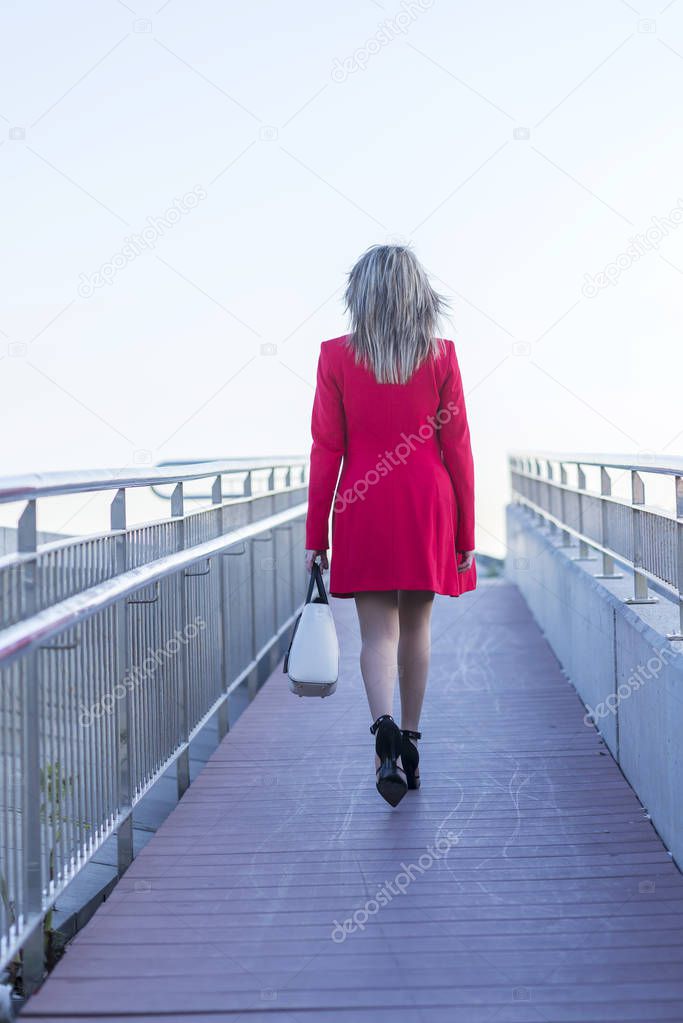 Elegant blonde woman wearing red jacket and skirt walking over the runaway to nowhere