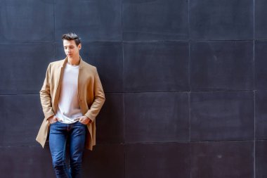 Sokağın ortasında kış giysileri giyen genç adam. Ceket, kot ve beyaz tatlı ile modern saç modeli ile genç adam.