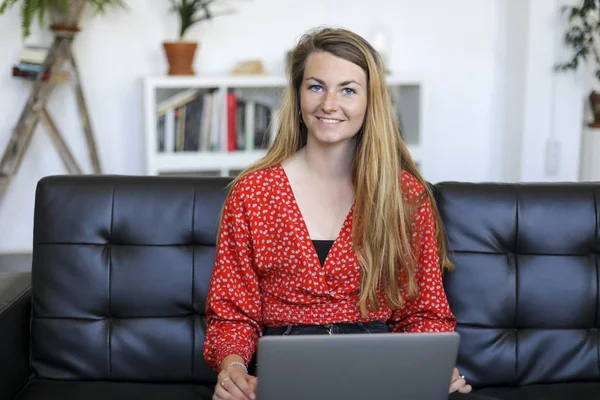 Entrepreneur woman wearing red shirt working with a laptop while sitting on a couch at home
