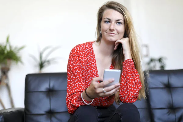 Bir Smartphone Kullanarak Deri Koltukta Otururken Gülümseyen Genç Sarışın Kız — Stok fotoğraf