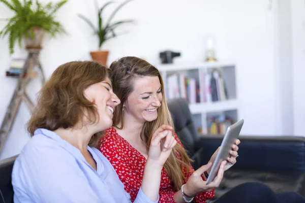 Overhead photograph of two beautiful young women at home sitting on sofa while using a tablet PC computer and smiling