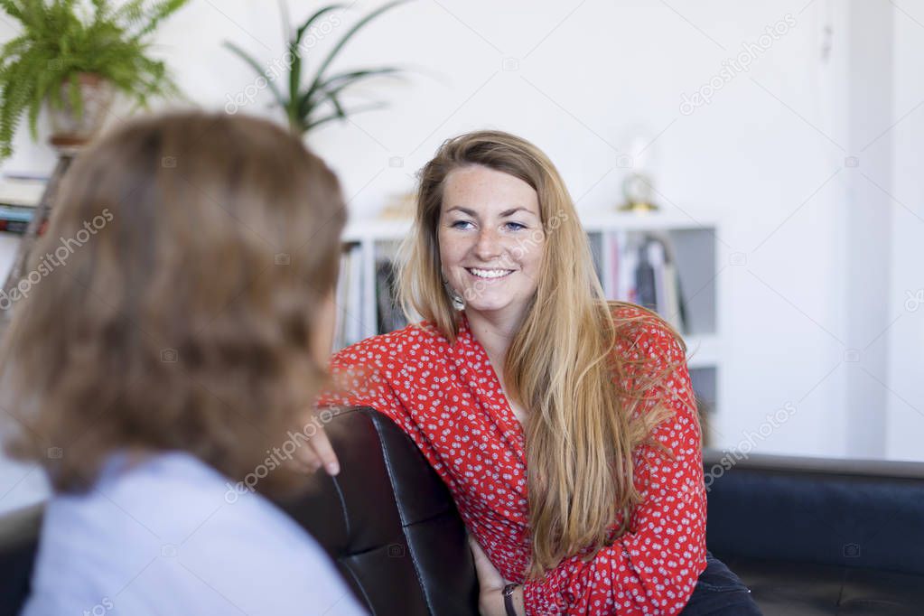 Two friends talking and laughing on a sofa in the living room at home