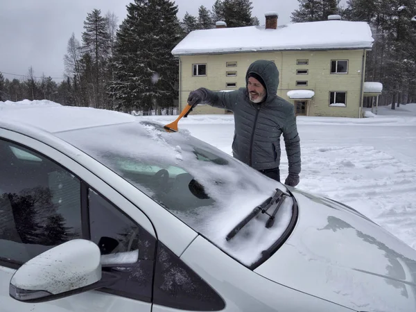 Man cleaning snow from car windshield with brush.Removing snow from car