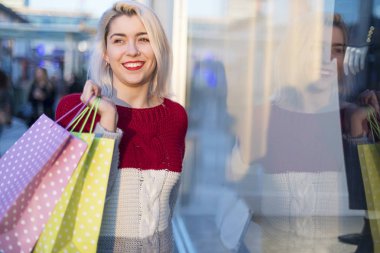 Kameraya bakarken bir alışveriş merkezinde duran bir gülümseyen genç kadın önden görünümü