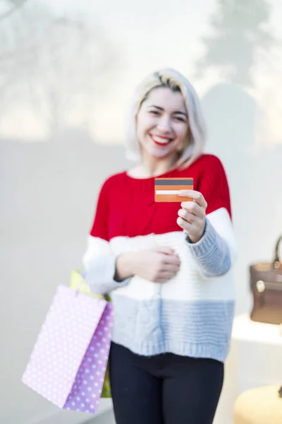 一个面带微笑的年轻女子拿着信用卡站在购物中心前看 — 图库照片