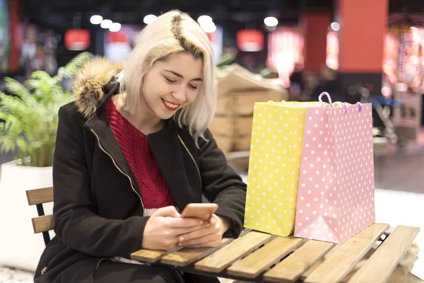 一个年轻的微笑的女人坐在咖啡吧 同时使用手机的侧视图 — 图库照片