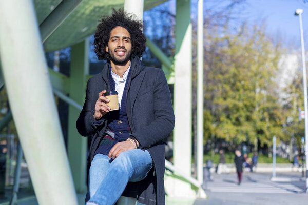 Hipster afro man standing with takeaway coffee, smiling pleasantly, standing on the city street. Millennial generation