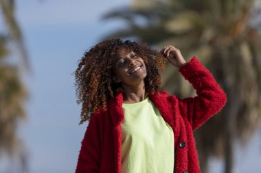 Gözlerini kapatma ve gülümseyen güneşli bir günde ise açık havada duran gülümseyen genç Afrika kadın önden görünümü