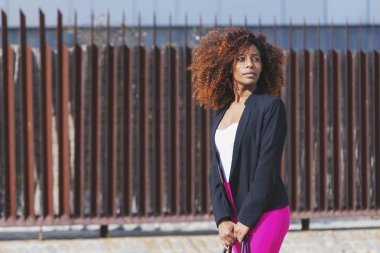 Şık giysileriyle ve çanta dururken sokakta güneşli bir günde giyen genç güzel kıvırcık kadın önden görünümü