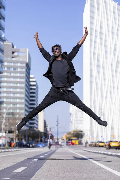 Jonge zwarte man het dragen van casual kleding springen in de stedelijke achtergrond. Lifestyle concept. Duizendjarige Afrikaanse man dragen van een zonnebril buiten — Stockfoto