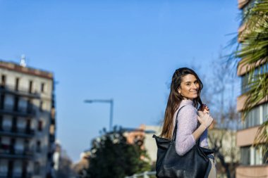 Güneşli bir günde görünümlü kamera ise sokakta duran gülümseyen güzel genç kadın, arkadan görünüş
