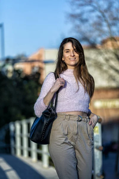 Εμπρόσθια όψη του χαμογελώντας όμορφη νεαρή γυναίκα με το χέρι στην τσέπη στέκεται στο δρόμο ενώ κάμερα που αναζητούν σε μια ηλιόλουστη ημέρα — Φωτογραφία Αρχείου
