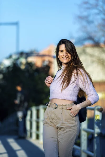 Vista frontal de sonriente hermosa joven mano en el bolsillo de pie en la calle mientras mira hacia otro lado en un día soleado — Foto de Stock