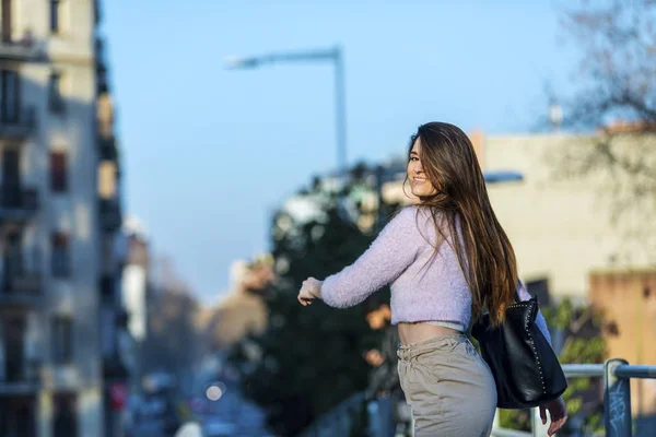Widok z uśmiechający się piękna młoda kobieta spaceru na ulicy, patrząc wstecz do aparatu w słoneczny dzień z tyłu — Zdjęcie stockowe