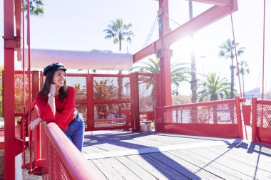 Güzel bir genç kadının uzakta açık havada parlak bir günde bakarken bir metalik köprü çit yaslanmış kentsel giyim eşyası Önden Görünüm