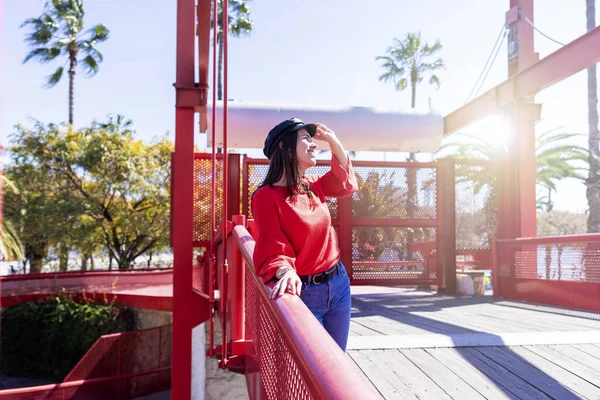 Vista frontal de una hermosa joven vestida con ropa urbana apoyada en una valla de puente metálico mientras mira al aire libre en un día brillante — Foto de Stock