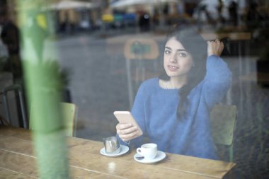 Genç güzel kadın kahve içme ve onun Smartphone kentsel kafede kapalı oturan kullanın. Cafe şehir yaşam tarzı. Güzel kız Casual portre